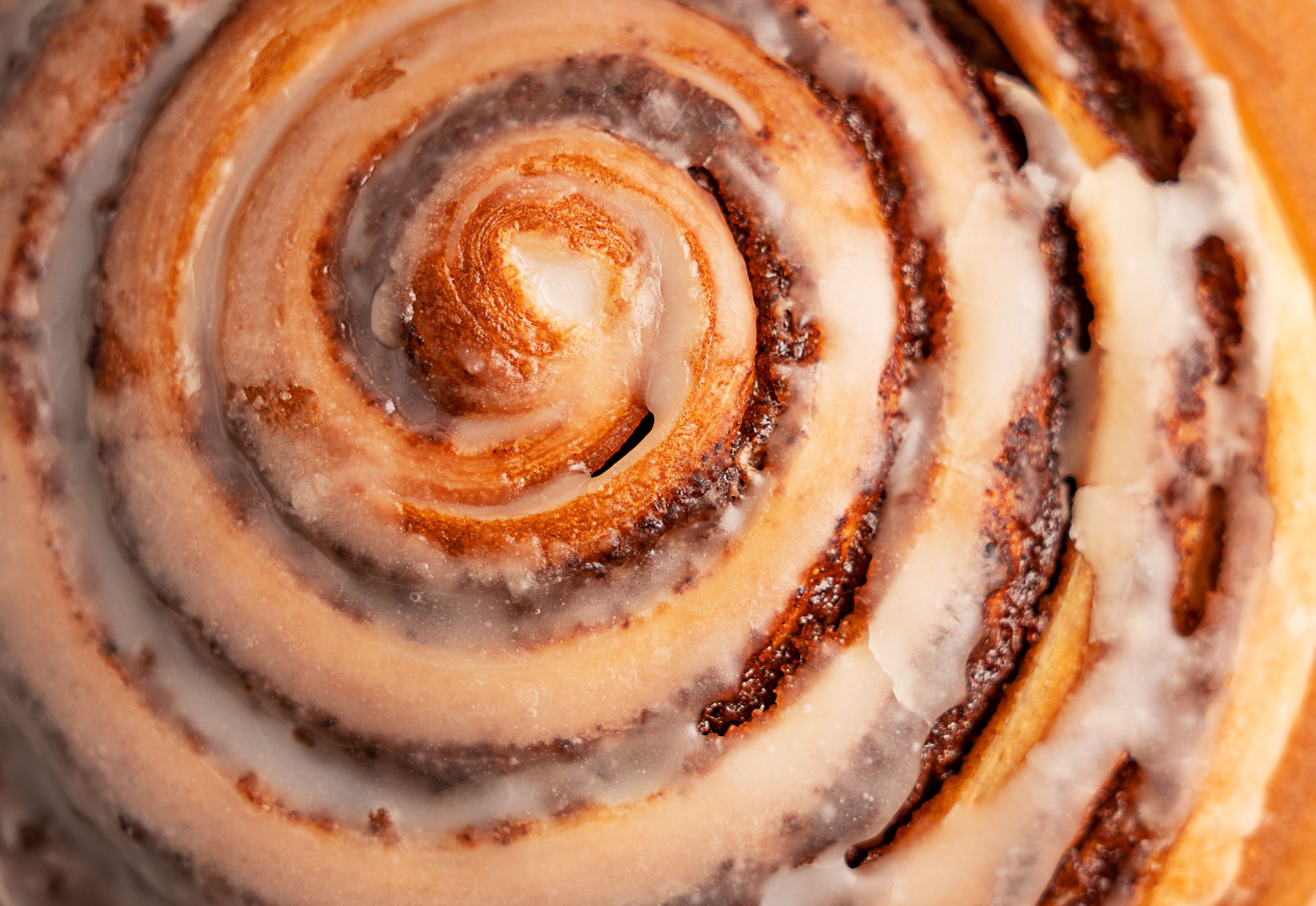 Background of close-up top view of a delicious cinnamon roll bun glazed with sugar icing
